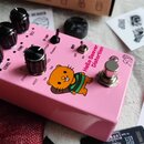 Růžový efekt pedál s nápisem Hello Beaver Distortion a obrázkem bobra. Na horní ploše jsou čtyři černé ovládací knoflíky s popisky LEVEL, TONE, DIST…