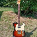 Elektrická kytara s tmelem v barvě sunburst, bílým pickguardem a hnedým hmatníkem. Na hlavě je nápis Squier. Tělo vykazuje známky opotřebení v podobě…