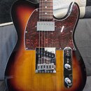 Elektrická kytara s tmelelovým povrchem v přechodové barvě od žluté přes oranžovou k hnědé. Nástroj má červený vzorovaný pickguard a chromované poten…