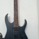 Elektrická kytara s matně černým povrchem a hnědým hmatníkem, umístěná na stěnovém držáku. Na hlavě je bílý nápis Ibanez. Nástroj má dva humbuckery,…