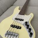 Krémově bílá elektrická basová kytara s pěti strunami a hnědým hmatníkem. Instrument má bílý perleťový pickguard a čtyři černé ovládací knoflíky. Na…