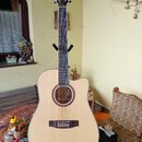 Akustická kytara s cutawayem, světlým topem a tmavým hmatníkem. Na hlavě je viditelné logo Epiphone. Nástroj je umístěn na černém stojanu v interiéru…