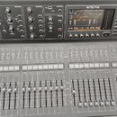 Šedý digitální mixovací pult značky MIDAS. Horní panel obsahuje několik sekcí s ovladači, displej a nápisy jako COMPU/PREAMP, EQUALISER, BUS SENDS, R…