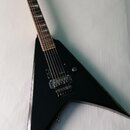 Černá elektrická kytara s ostrým, V-tvarovým korpusem a tmavým hmatníkem s bílými vložkami. Nástroj má dva humbuckery, jeden ovládací knoflík a fixní…