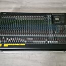 Černý mixovací pult umístěný v transportním kufru. V horní části je vlevo logo YAMAHA a vpravo nápis MGP32X. Na spodní hraně jsou nalepené žluté štít…
