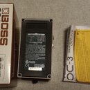 Fotografie zobrazuje krabici, napájecí adaptér a dokumentaci k efektu BOSS OC-3 SUPER Octave. Na bílé krabici je hnědý nápis BOSS a model OC-3 SUPER…