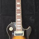 Elektrická kytara typu Les Paul s barevným přechodem od žluté přes oranžovou k černé (sunburst). Na hlavě hmatníku je bílý nápis Gibson a pod ním pod…