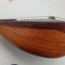Detailní pohled na dřevěné tělo strunného nástroje s hnědým lakem. Povrch je tvořen řadou úzkých dřevěných lišt, které vytvářejí žebrovaný tvar. Lak…
