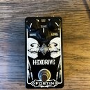 Černý kytarový efekt s bílým grafickým motivem dvou lebek a hvězdy. Na pedálu jsou tři ovládací knoflíky s popisky DRIVE, TONE a LEVEL a nápisy HEXDR…