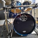 Modrá bicí souprava s chromovaným hardwarem a stojanem značky Millenium. Na přední straně basového bubnu je bílý nápis SINCE 2004 DC DRUMS QUALITY HA…