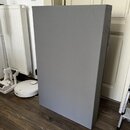 Na fotografii je šedý textilní kryt nebo obal obdélníkového tvaru, který stojí vertikálně na dřevěné podlaze. Povrch látky je hladký a bez viditelnýc…