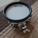 Bílý tréninkový pad s černým gumovým okrajem a chromovaným kovovým základnami. Na povrchu je černý nápis „drum-tec“ v oválu a pod ním menší text „des…