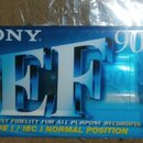 Modrá plastová kazeta s nápisem SONY v levém horním rohu a číslem 90 v pravém horním rohu. Uprostřed je velký stříbrný nápis EF. Dole jsou texty EXCE…