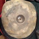 Kulatý činel značky Zildjian s matným, hnědový povrchem. Na povrchu je vidět tmavé logo Zildjian a v centru malý bílý štítek s čárovým kódem. Povrch…