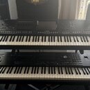Dvě černé digitální klavírní aranžéry umístěné na stojanu nad sebou. Horní nástroj nese nápisy YAMAHA a Genos2. Dolní nástroj je širší, má klávesnici…