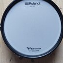 Fotografie znázorňuje elektronický buben s bílou membránou a černým obručem. Na horní části membrány je nápis Roland MESH HEAD a v dolní části V-Drum…