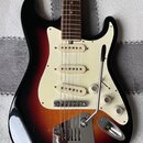 Elektrická kytara s trupem v černo-oranžovém sunburst provedení a bílým pickguardem. Nástroj má tři bílé snímače typu single-coil a hnedý hmatník. Na…