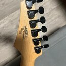 Zadní strana hlavy kytary z přírodního dřeva se šesti černými ladicími kolíky. Na dřevě je černý nápis: CE RoHS Compliant, Serial Number 101133820, M…