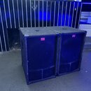 Dva černé, hranaté reproduktorové boxy s povrchem z tmavé textury. Na přední straně každého boxu je mřížka a červený obdélníkový štítek s bílým nápis…