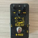 Černý efekt pedál s texturovaným povrchem. Na přední straně jsou tři ovládací knoflíky s popisky FUZZ, BIAS a VOLUME. Uprostřed je žluté logo s obráz…
