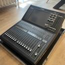 Černý digitální mixovací pult značky YAMAHA, model QL1. Zařízení je umístěno v transportním kufru s hliníkovými hranami, na kterém je nápis YAMAHA. P…
