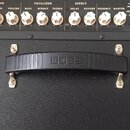 Detailní pohled na ovládací panel a horní část černého kytarového komba. Na panelu jsou bílé oválné knoflíky a nápisy včetně značek Nextone Stage a B…