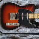 Elektrická kytara typu Telecaster v barevném přechodu od červené přes oranžovou k černé s černým pickguardem a javorovým hmatníkem. Nástroj je umístě…