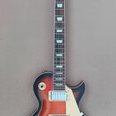 Elektrická kytara s trupem v červeno-oranžovém sunburst provedení a černou hlavou. Na hlavě je bílý nápis Blond. Nástroj má dva humbuckery s bílými k…