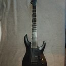 Černá elektrická kytara s matným povrchem a špičatou hlavou. Na hlavě je bílé logo Ibanez, na hmatníku je v 12. pražci nápis Ibanez. Nástroj má jeden…
