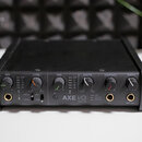Černý audio rozhraní s nápisem AXE I/O SOLO. Přední panel obsahuje šest otočných ovladačů s popisky GAIN, Z-TONE, GAIN, MONITOR, HEADPHONES a MASTER,…