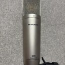 Stříbrný kondenzátorový mikrofon s kovovou síťkou v horní části. Na těle je uveden nápis M-AUDIO a dále text NOVA CLASS A FET. Mikrofon je umístěn v…