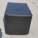 Černý subwoofer s hranatým tvarem a texturovaným povrchem. Přední strana je kryta kovovou perforovanou mřížkou, na které je v dolní části umístěno lo…