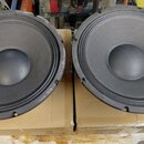 Dva černé kruhové reproduktory položené na hnědých kartonových krabicích. Mají černou membránu s výrazným žebrováním a centrálním kalotou. Na viditel…