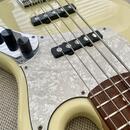 Detail elektrické basové kytary v krémové barvě s bílým perleťovým pickguardem. Nástroj má dva černé snímače, chromovaný most a dva černé oválné knof…