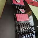 Černá elektrická kytara s dvěma červenými humbuckery. Na spodním snímači je viditelné logo emg a na kobylce nápis GOTOH JAPAN. Na těle kytary jsou dv…