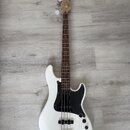 Bílá elektrická basová kytara se čtyřmi strunami, černým pickguardem a hnědým hmatníkem. Na hlavě je viditelné logo "Squier". Nástroj vykazuje známky…