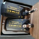 Dvě černé bezdrátové vysílače/přijímače s 6,3mm jack konektory v kartonové krabici. Na obou zařizeních je žlutý štítek s nápisy „MADE IN CHINA“, „FCC…