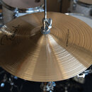 Zlatý kovový činel s koncentrickými rýhami na povrchu. Na pravé straně je svislý nápis "Zildjian 14" SOUND EDGE HIHAT". V levé části je černý ruční p…