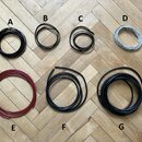 Fotografie zobrazuje sedm navinutých kabelů v různých barvách a délkách, označených písmeny A až G. Kabely A, B, C, F a G jsou černé, kabel D je svět…