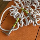 Bílý spirálový instrumentální kabel s chromovanými 6,3mm konektory. Na kabelu jsou dva žluté nápisy: „INSTRUMENT“ a „KORG-BITE“. Povrch kabelu i kone…