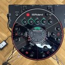 Černý kruhový mixážní pult značky Roland s modelem SESSION MIXER HS-5 a nápisem MAIN MIX. Zařízení obsahuje několik úrovní ovládacích knofíků, posuvn…