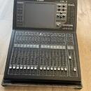 Černý digitální mixážní pult značky YAMAHA, model QL1. Zařízení obsahuje dotykový displej, řadu posuvníků s číslováním 1 až 16 a ovládací tlačítka. P…