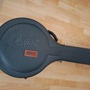 Černý tvrdý kufýr na hudební nástroj s rukojetí. Na povrchu je vyražený nápis „Epiphone“ a přišitý hnědý kožený štítek s textem „Accessories & More I…