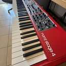 Červený digitální klavír s bílými a černými klávesami. Na boku je bílý nápis „nord stage 4 HAMMER ACTION 88“. Horní panel obsahuje množství ovládacíc…
