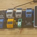 Na černém pedalboardu je umístěno sedm efektů pro kytaru. V horní řadě jsou tři stříbrné pedály s nápisy Noise Suppressor, Digital Delay a modrý peda…