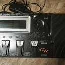 Černý kytarový syntetizátor s nápisem Roland GR-55 GUITAR SYNTHESIZER. Zařízení má displej, ovládací knoflík a několik tlačítek s popisky jako SOUND…