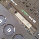 Černý pad kontrolér s nápisy Roland, PAD-MIDI INTERFACE a PM-16. Zařízení obsahuje řadu posuvníků, displej a kulaté gumové pady s bílými označením 3,…