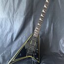Černá elektrická kytara s tělem ve tvaru V a žlutými konturními pruhy. Na hlavě hmatníku je bílý nápis Jackson. Nástroj má dva humbuckery, dva ovláda…