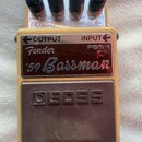 Efektový pedál v béžovém provedení s hnědým spínacím tlačítkem. Na pedálu jsou nápisy OUTPUT, INPUT, Fender FBM-1 a '59 Bassman. Na spínacím tlačítku…