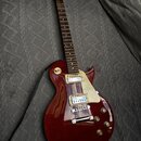 Tmavě červená elektrická kytara s tvarem singlecut a krčkem z tmavého dřeva. Na těle jsou dva humbuckery s krémovými kryty a krémový pickguard. Na hl…